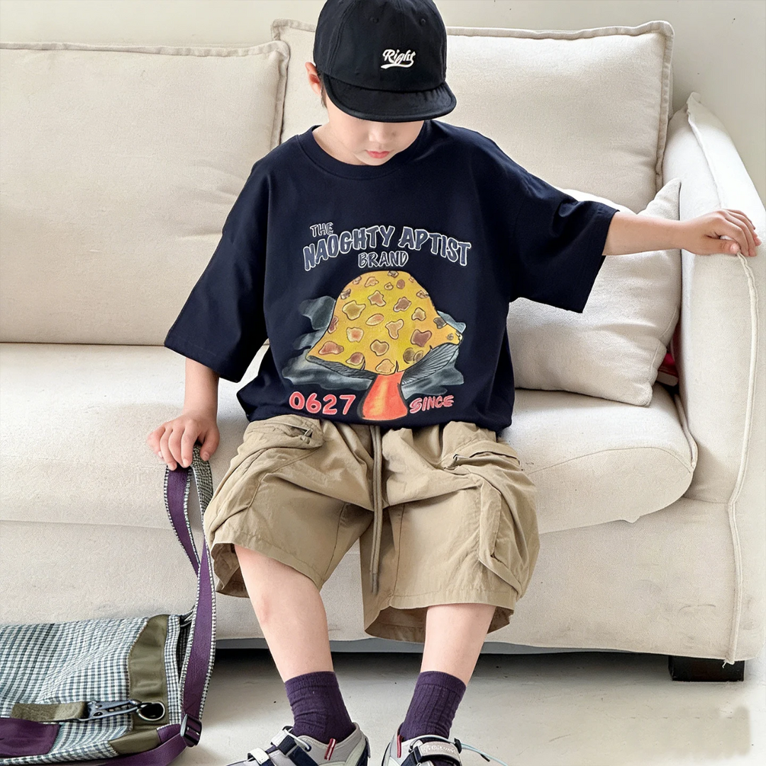 Child wearing the black mushroom graphic T-shirt while seated beside a sofa