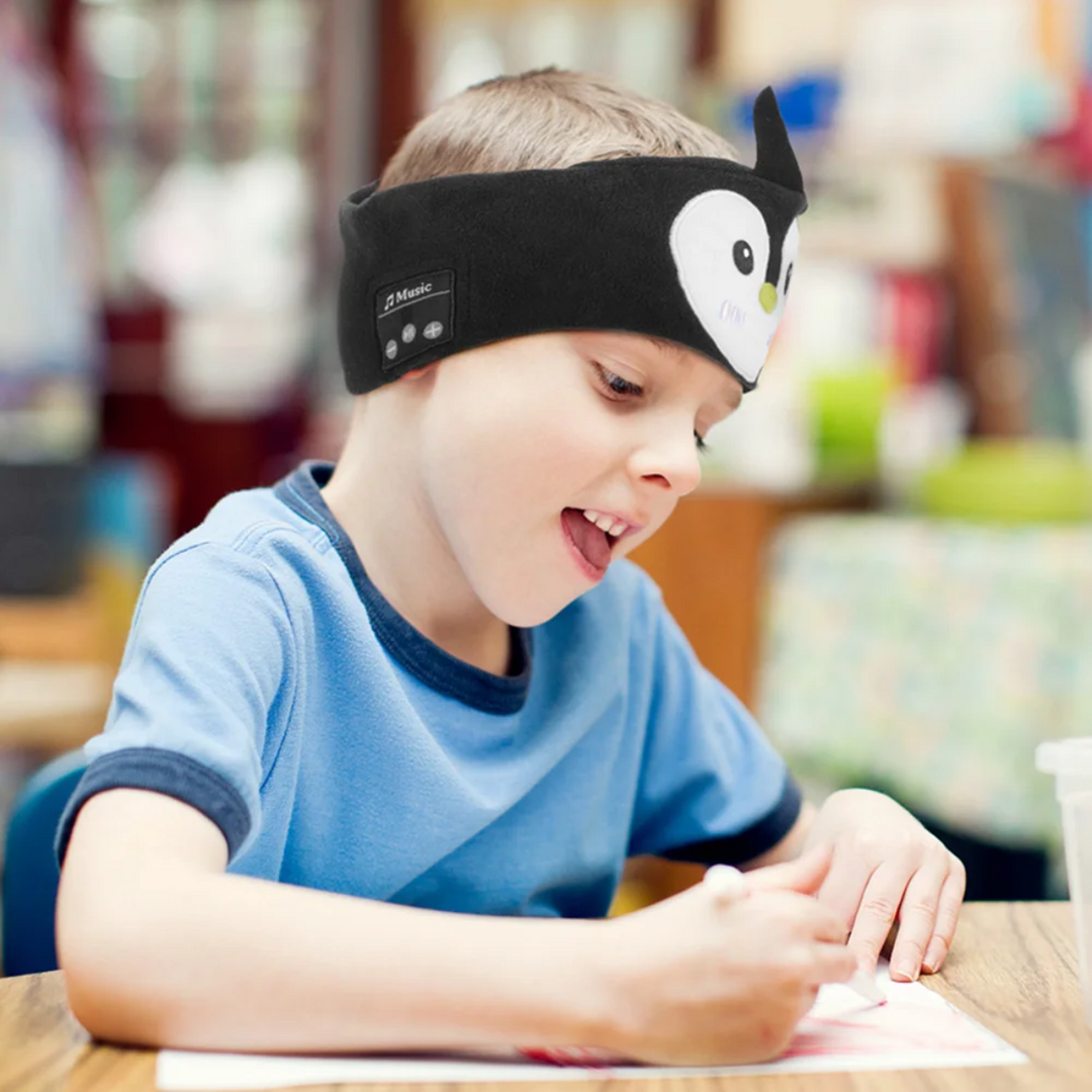 Child at a table wearing the black penguin Bluetooth sleep mask as a headband.