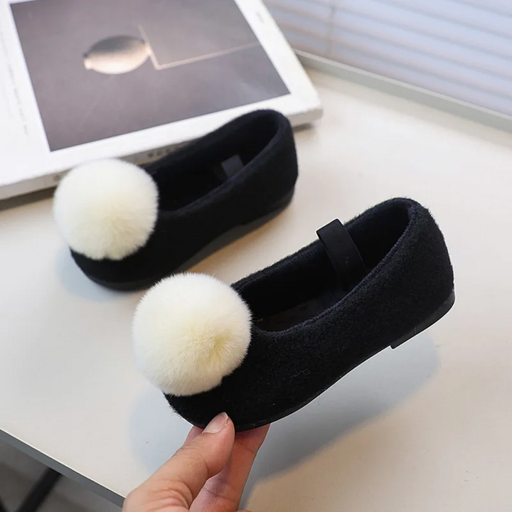 Black ballet flats with contrasting light pom-poms and black elastic straps