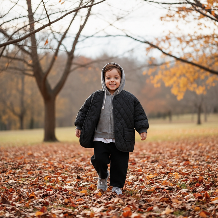 Child wearing a black quilted jacket over a gray hooded top outdoors