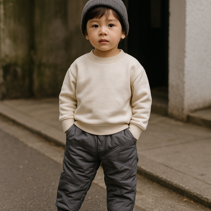 Child wearing black quilted winter pants and a cream sweater outdoors