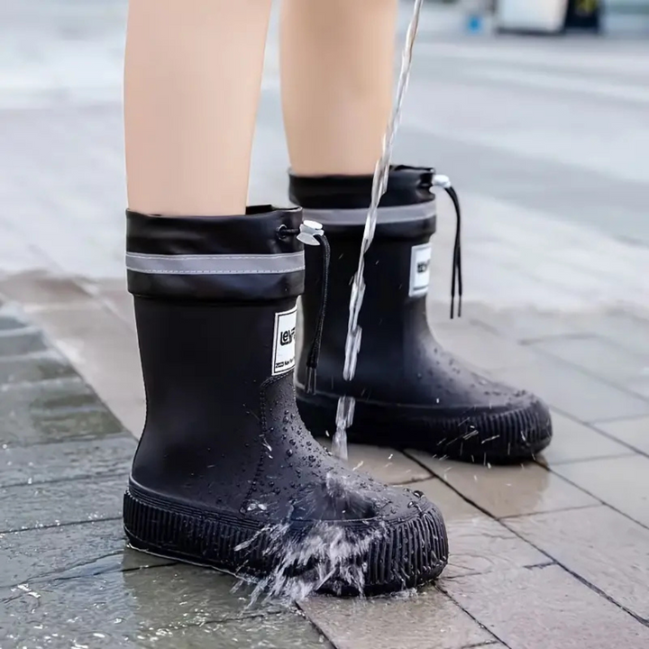 Water splashing over black rain boots on wet paving