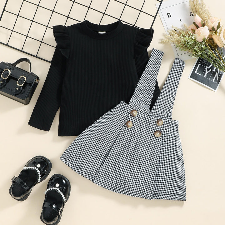 Black ribbed long-sleeve top laid beside a houndstooth pinafore skirt with four decorative buttons.