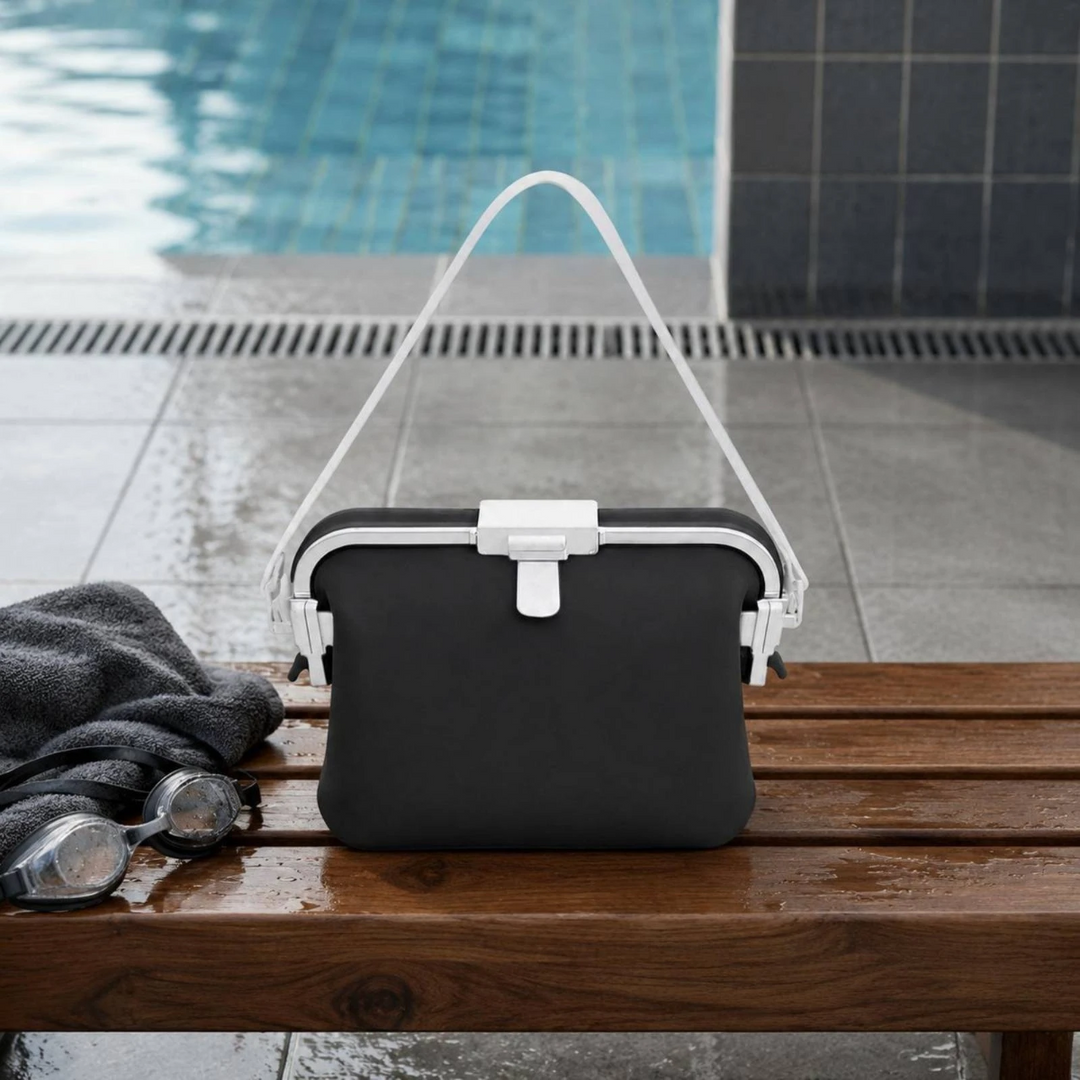 Black silicone shoulder bag with a white strap on a poolside bench.
