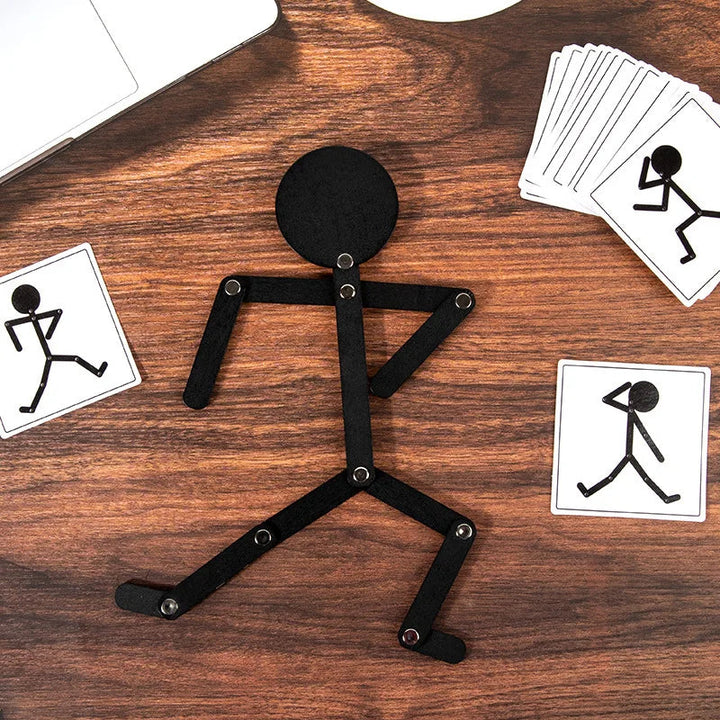 Black jointed stick figure on a wooden surface with black-and-white pose cards