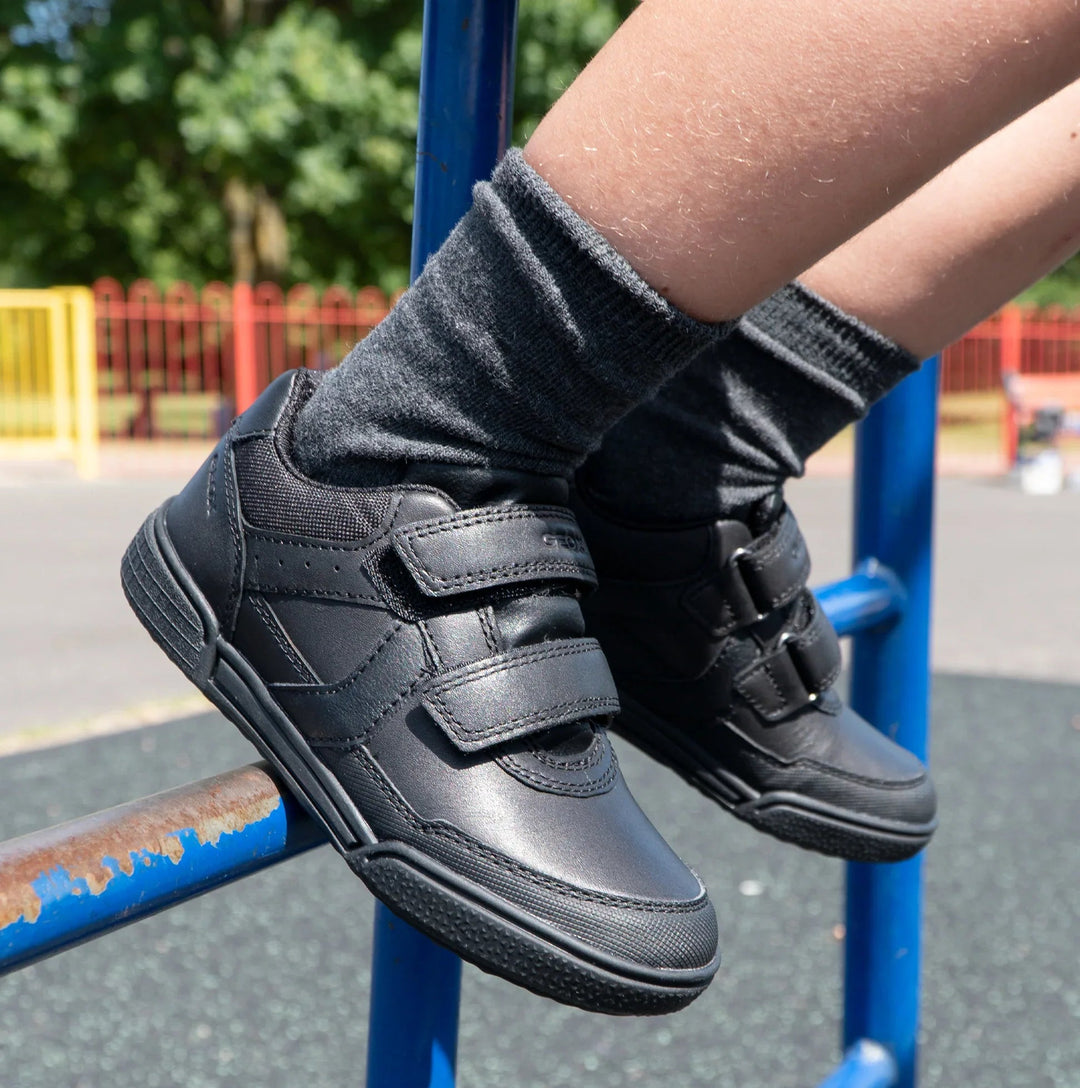 Child wearing black double-strap sneakers and gray socks on a playground rail