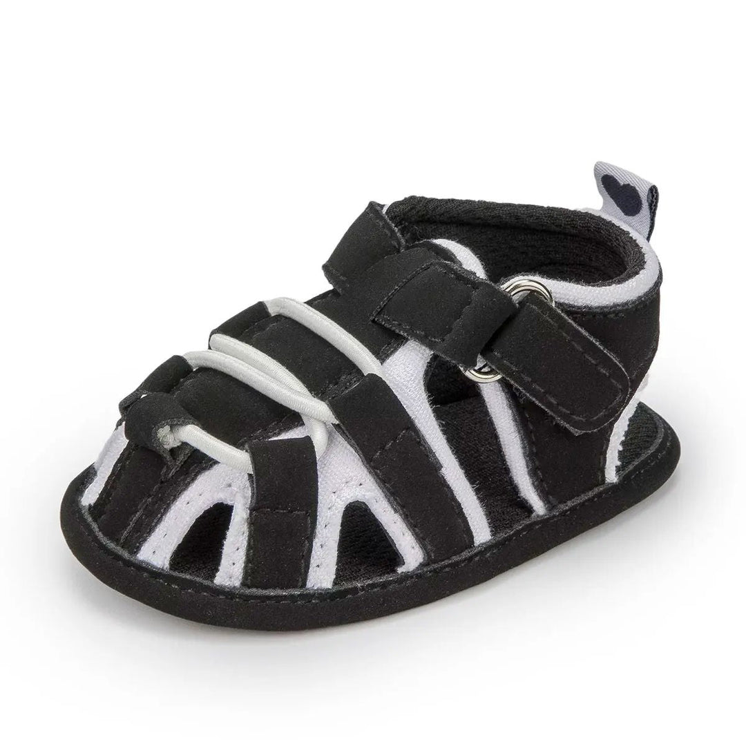 Black baby sandal with white trim, front cords and an ankle strap