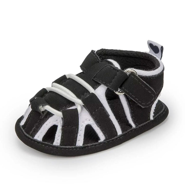 Black baby sandal with white trim, front cords and an ankle strap