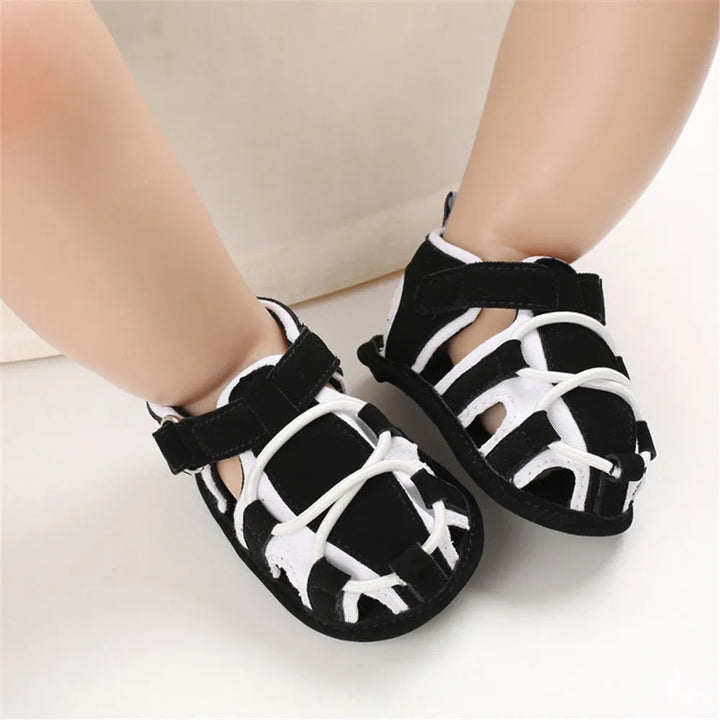 Black and white strappy baby sandals worn on a child&