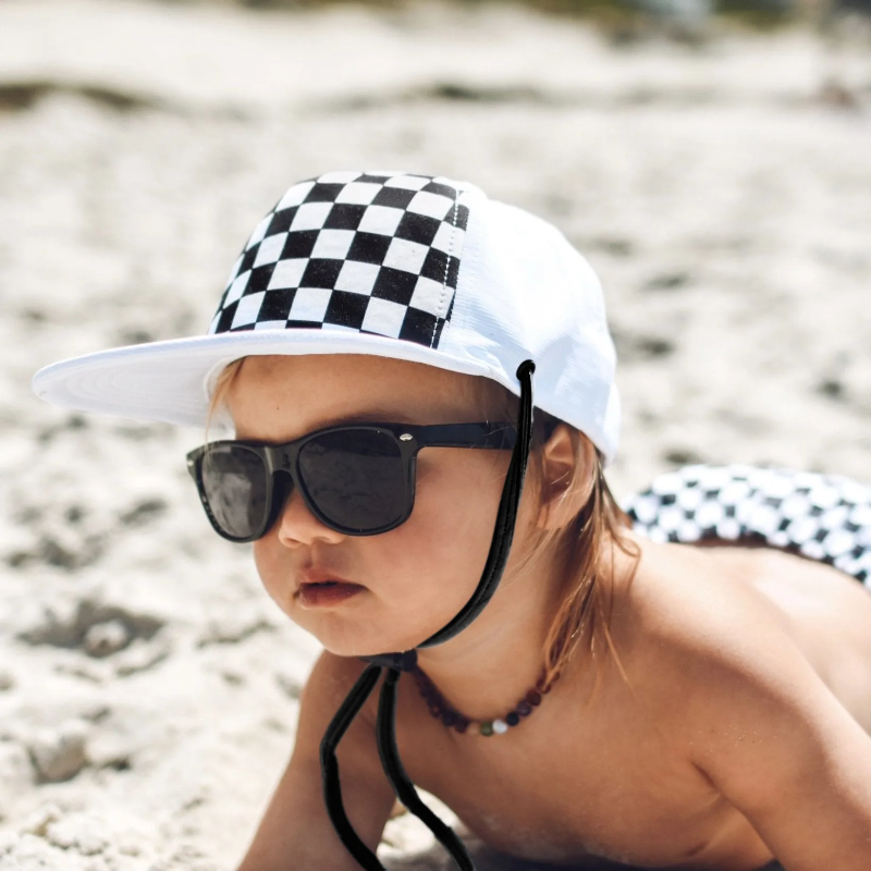 Child wearing a white cap with a black-and-white checkerboard front and black chin strap