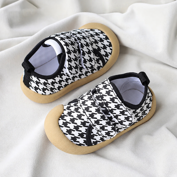 Black-and-white houndstooth baby sneakers with tan soles on white fabric