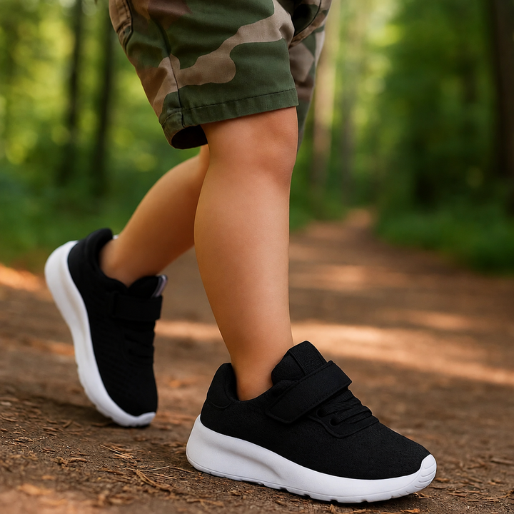 Child wearing black mesh sneakers with white soles on a wooded path