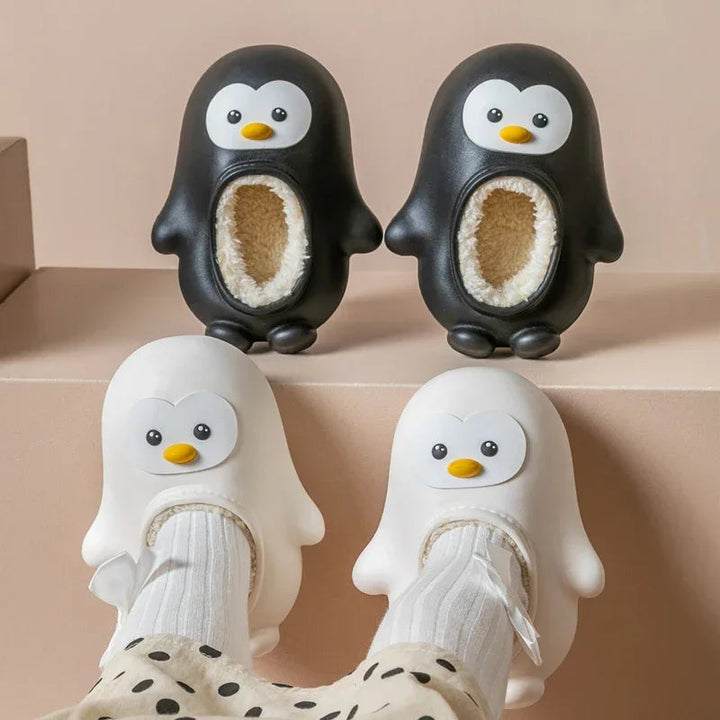 Black penguin slippers on a ledge above white penguin slippers worn with socks