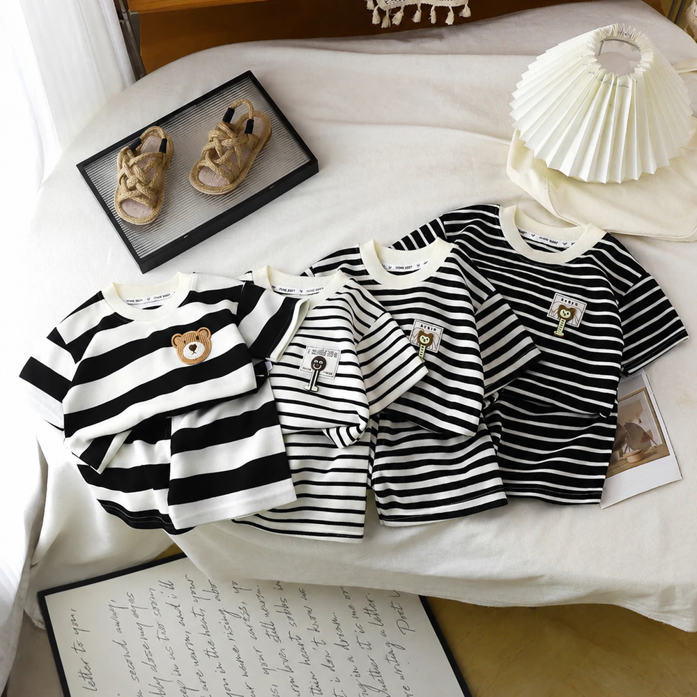 Black-and-white striped children's T-shirts arranged on a bed with contrasting stripe widths.