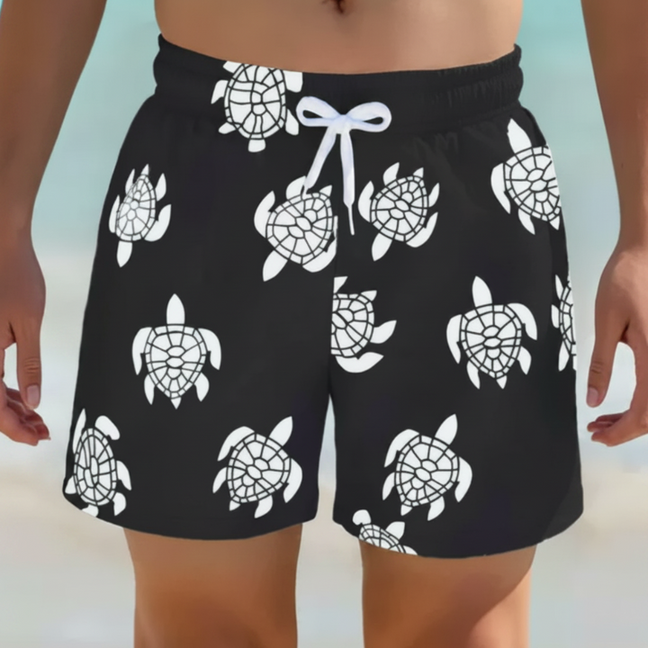 Black swim trunks with white turtle prints and a white drawstring, shown from the front