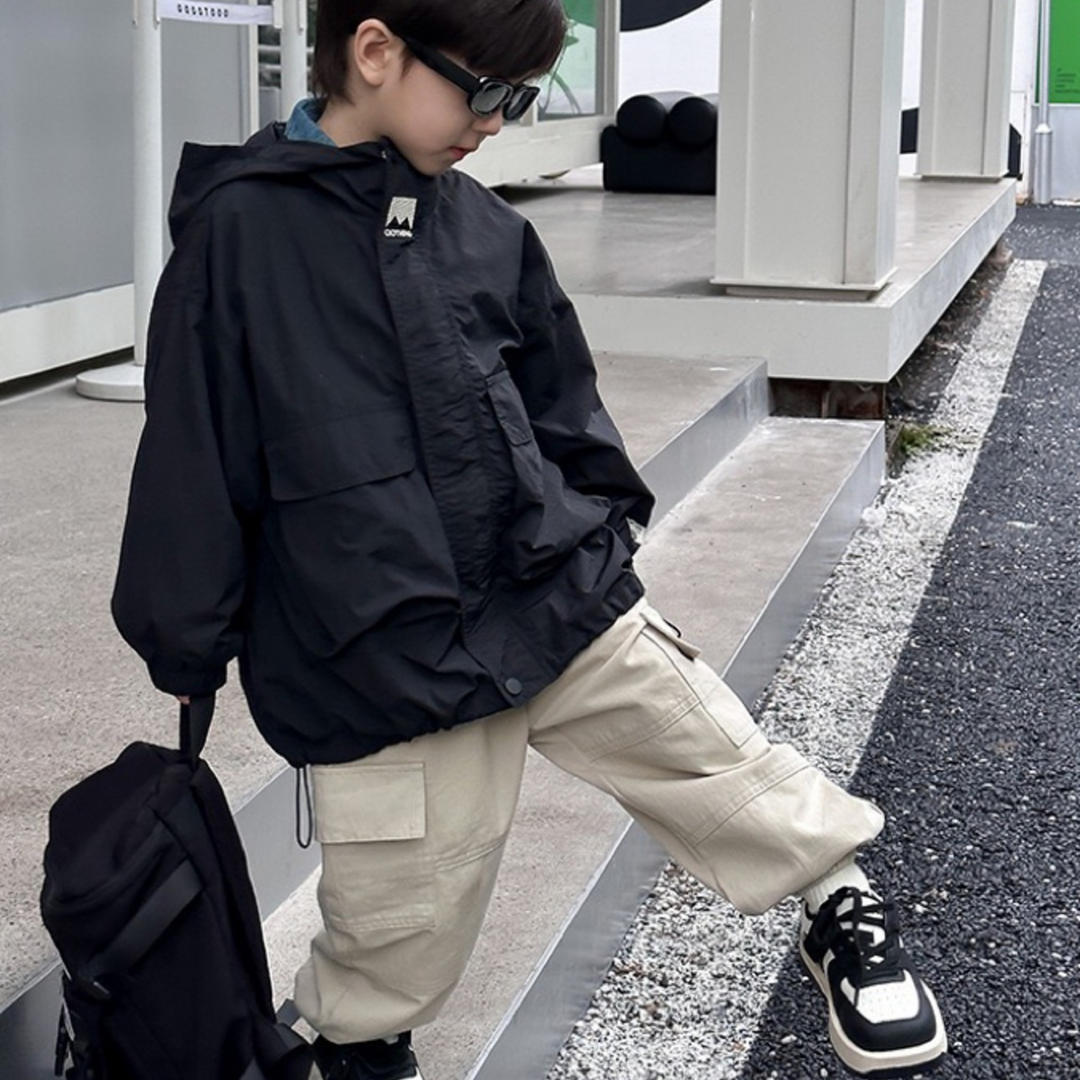 Child wearing a black windbreaker with beige pants on outdoor steps