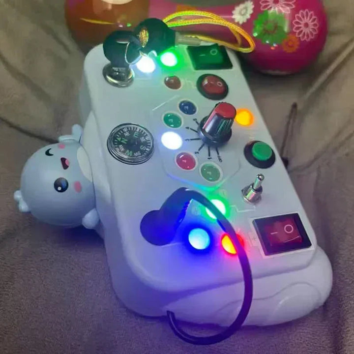 Light blue activity board with colored lights glowing beside buttons, switches, and a dial