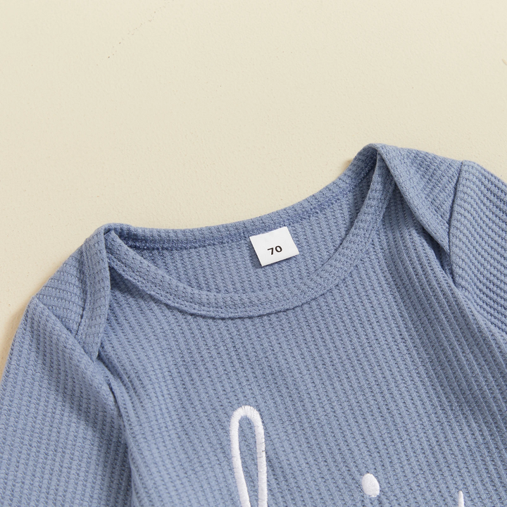 Close-up of the overlapping shoulder neckline and ribbed fabric on a blue baby jumpsuit