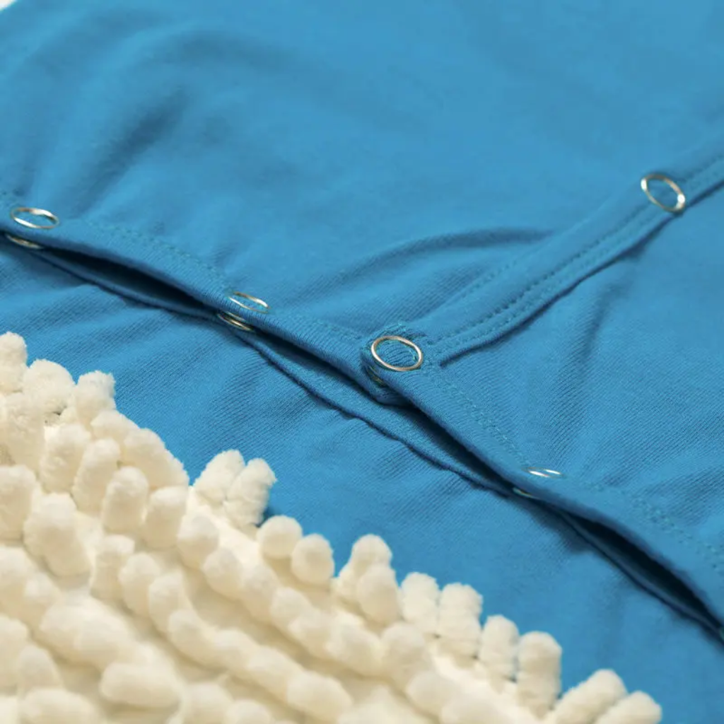 Close-up of snap closures on a blue baby jumpsuit beside white cleaning fibers