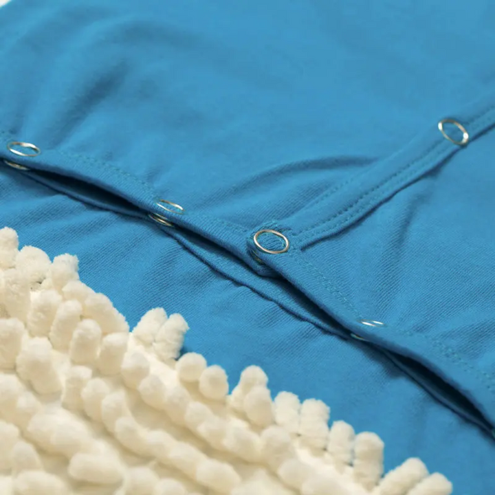 Close-up of snap closures on a blue baby jumpsuit beside white cleaning fibers