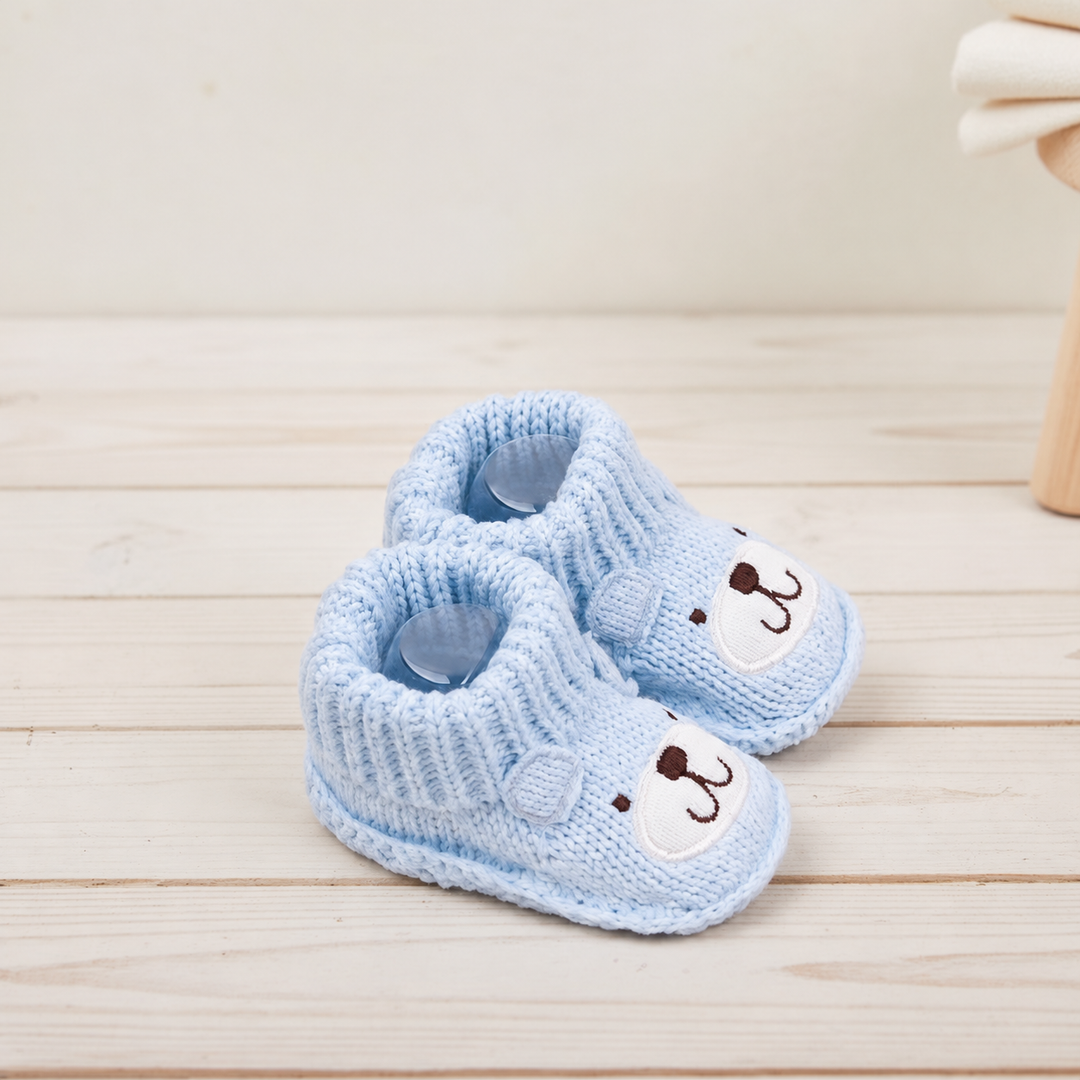 Angled view of light blue bear baby booties on a pale wooden surface