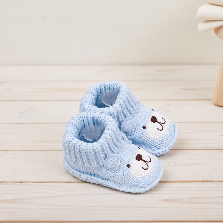 Angled view of light blue bear baby booties on a pale wooden surface