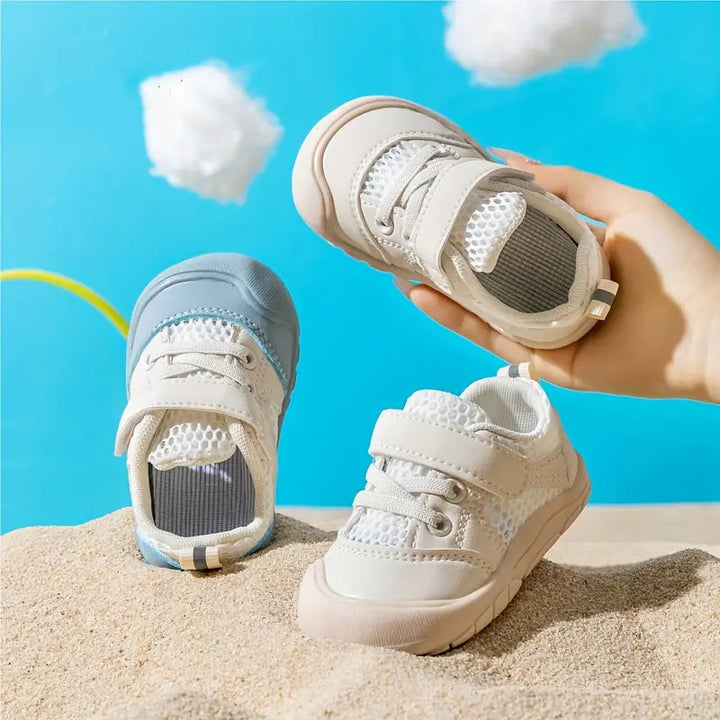 Blue and beige mesh baby shoes on a sand display, showing rounded toes and adjustable straps