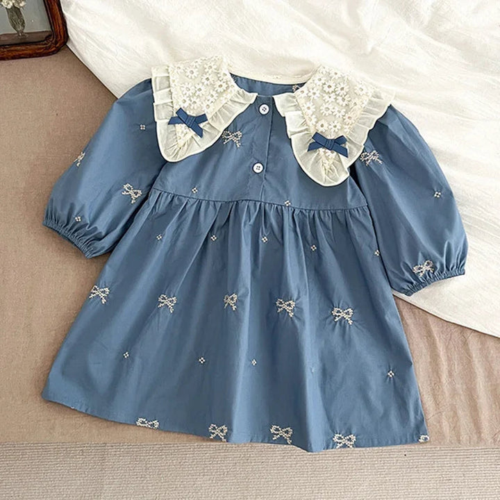 Blue bow-embroidered dress laid flat, showing the cream collar and button-front bodice