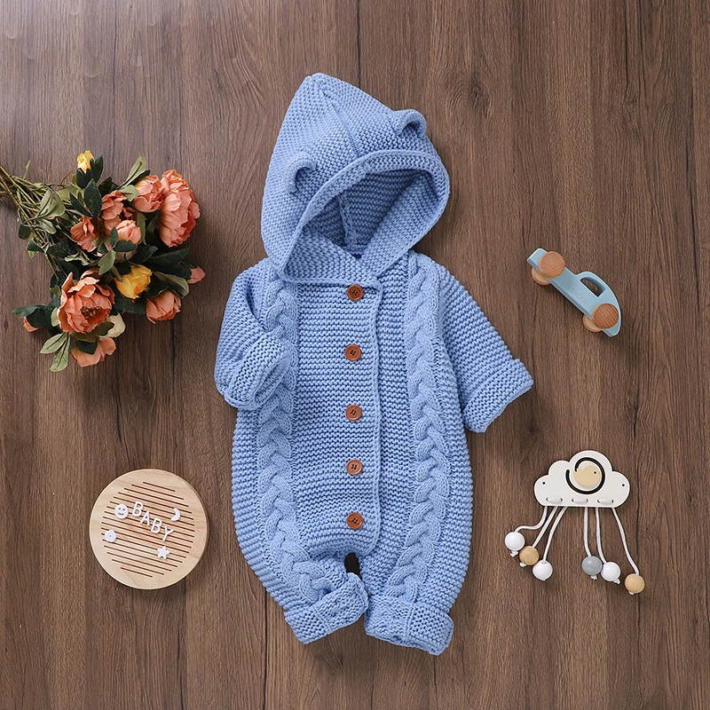 Blue cable-knit baby jumpsuit with a button front and ear-detail hood laid flat on a wooden surface