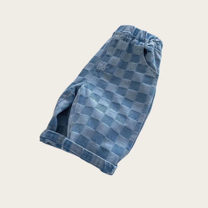 Angled side view of blue checkerboard pants with a gathered waist and turned-up hems
