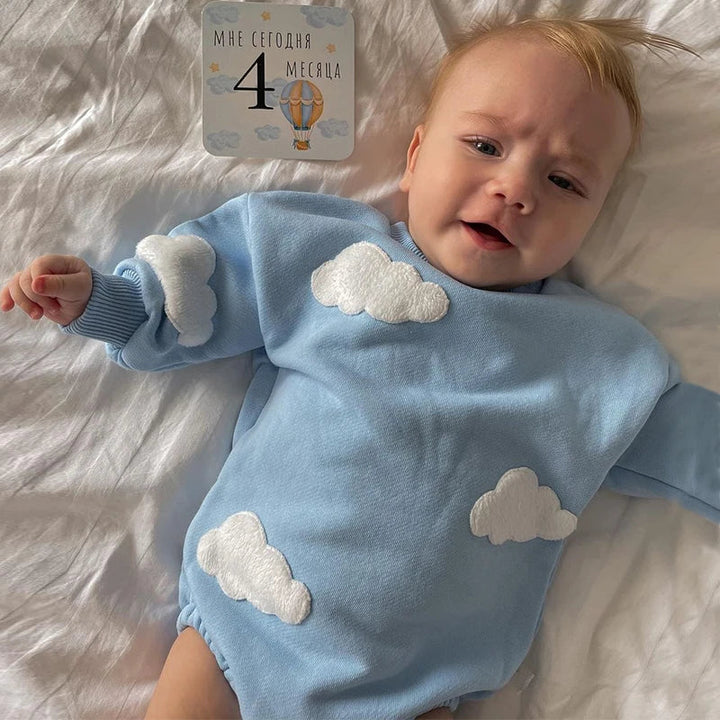 Baby wearing a blue sweatshirt romper with raised white cloud details.