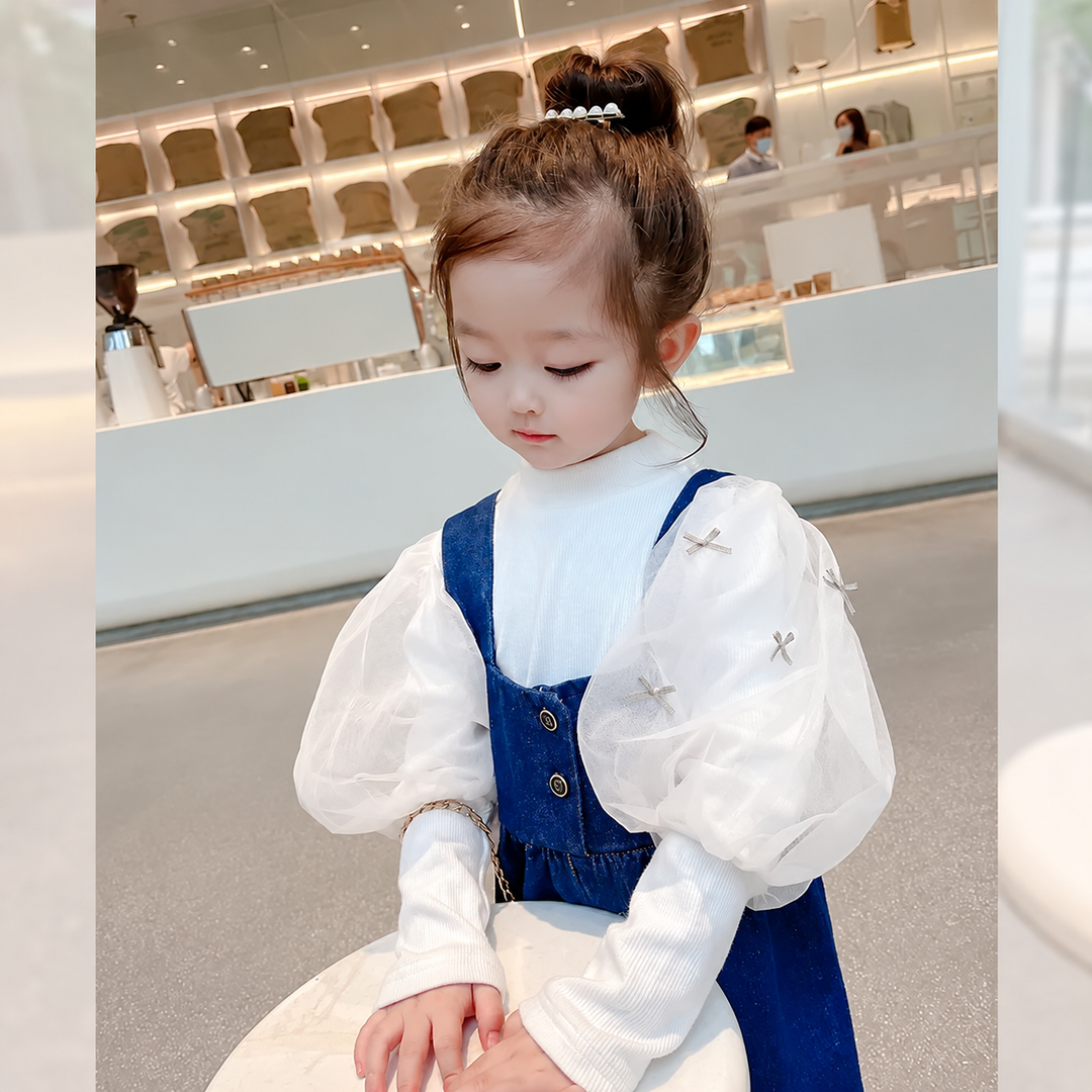 Close view of the front bib and straps on blue cotton overalls over a white blouse