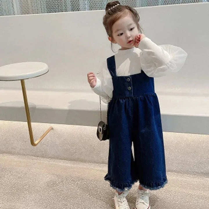Child wearing blue cotton overalls over a white puff-sleeve blouse