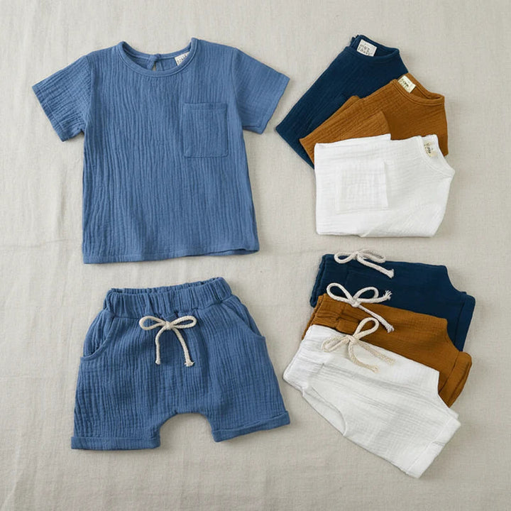 Blue cotton T-shirt and shorts laid flat beside folded navy blue, brown, and white pieces.
