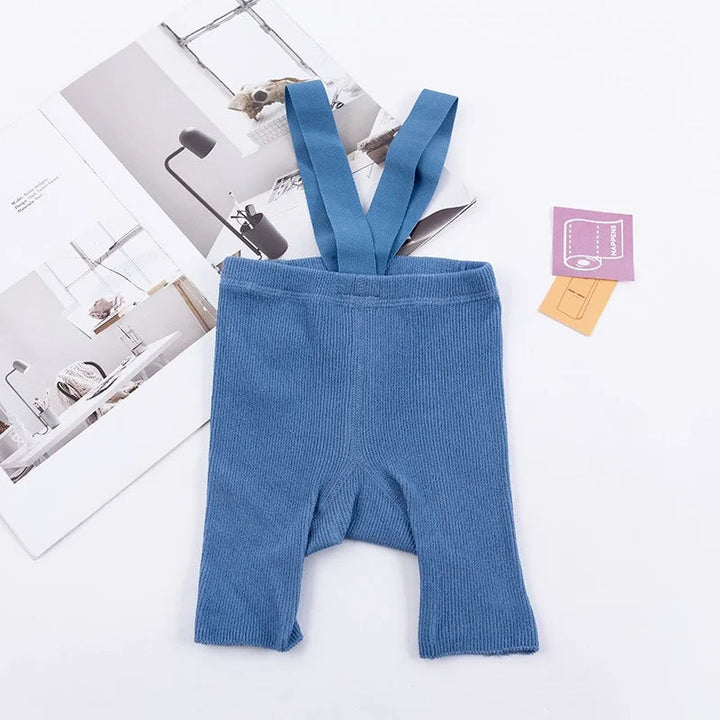 Blue ribbed suspender shorts laid flat with matching shoulder straps.