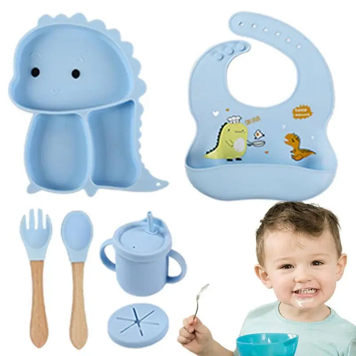 Blue dinosaur tableware set with bib, handled cup, utensils, and a child holding a spoon