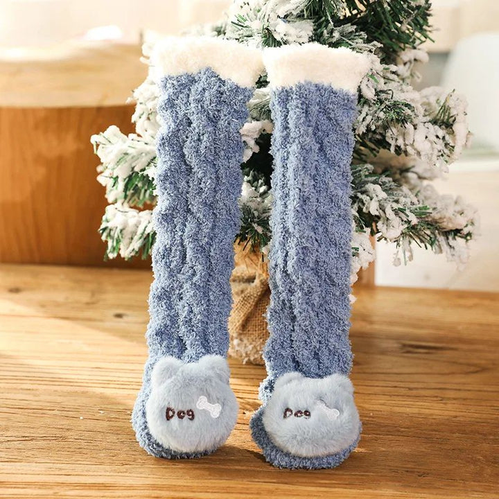Blue long baby socks with dog faces and cream cuffs standing beside a small tree.
