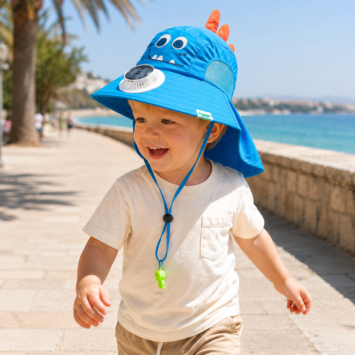 Child wearing a blue dinosaur fan hat with a neck flap on a seaside walkway.