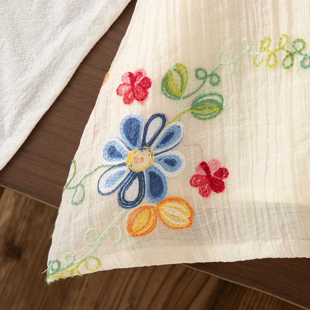 Blue flower embroidery and green stitching near the hem of the cream summer dress