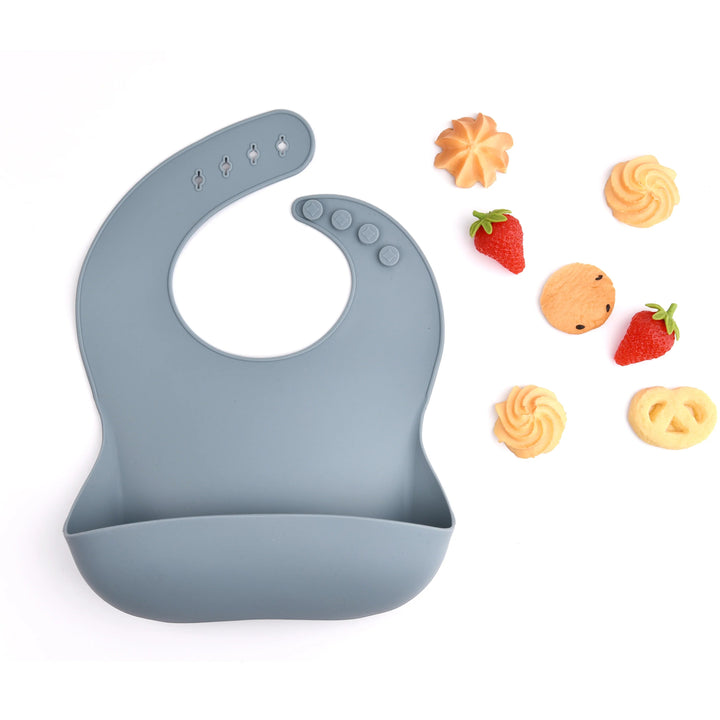 Blue-gray silicone bib with a front pocket, shown beside strawberries and small snacks.