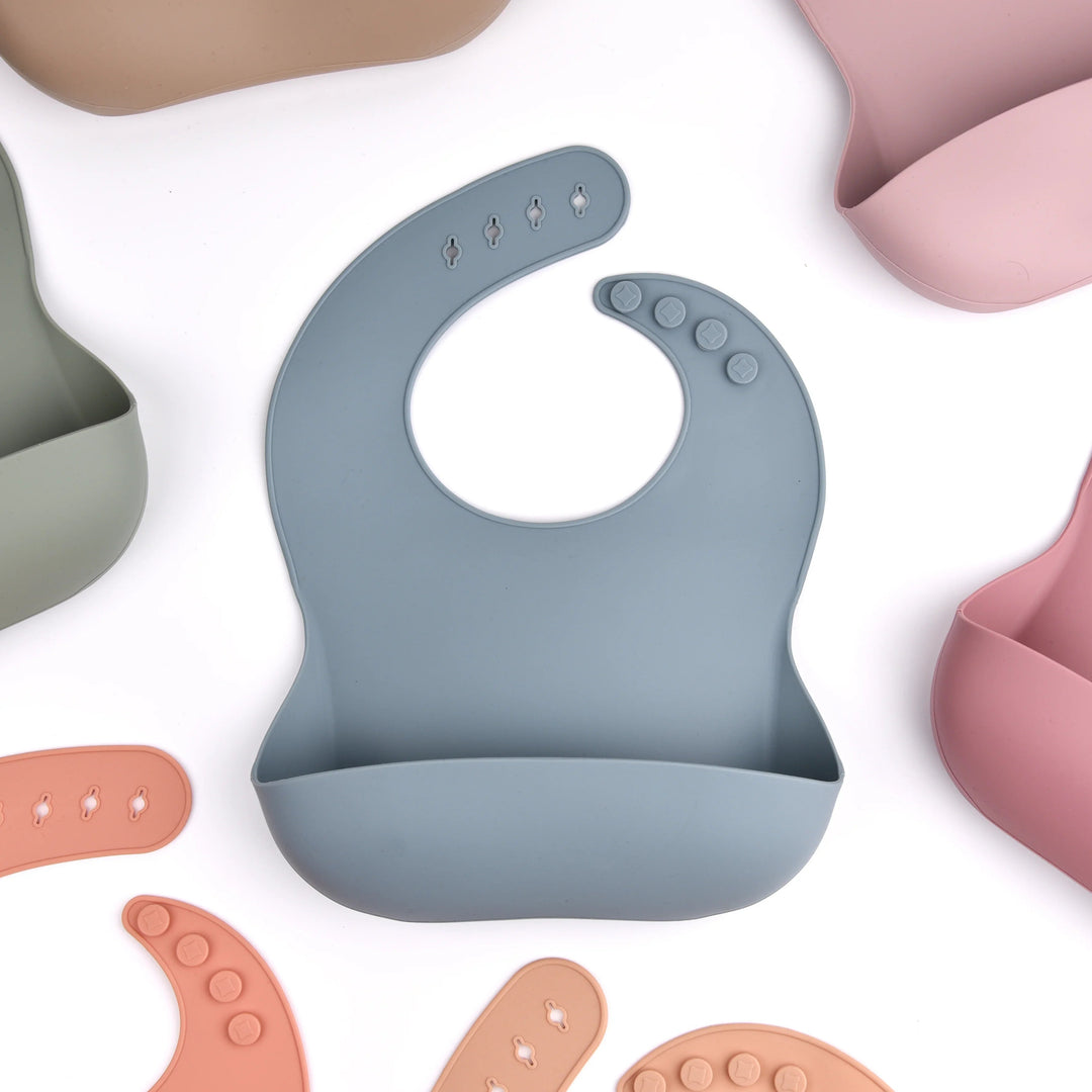 Blue-gray silicone bib with a front pocket, surrounded by bibs in muted colors.