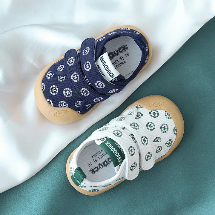 Navy and white-and-green printed baby sneakers with strap closures and tan toe caps