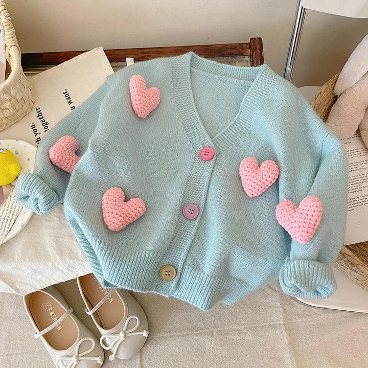 Blue V-neck cardigan with raised pink hearts, colorful buttons, and rolled cuffs