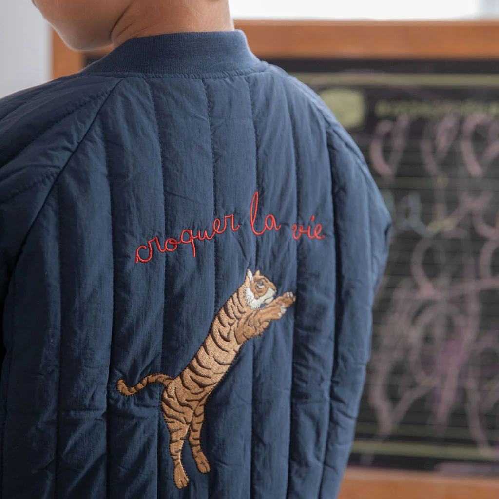 Close-up of tiger embroidery and red lettering on the back of the blue quilted jacket