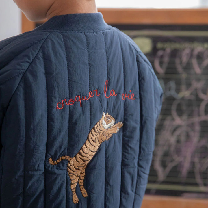 Close-up of tiger embroidery and red lettering on the back of the blue quilted jacket