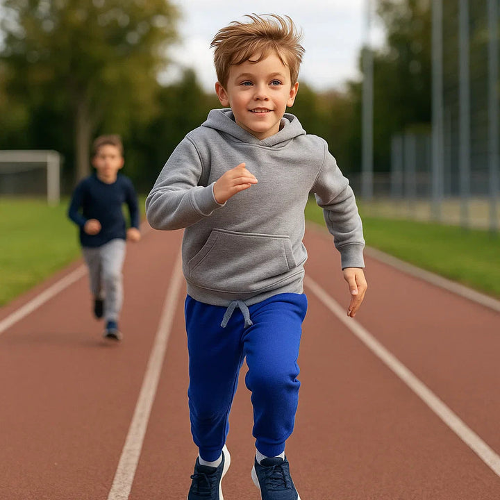 Child running on an outdoor track in blue joggers and a gray hoodie
