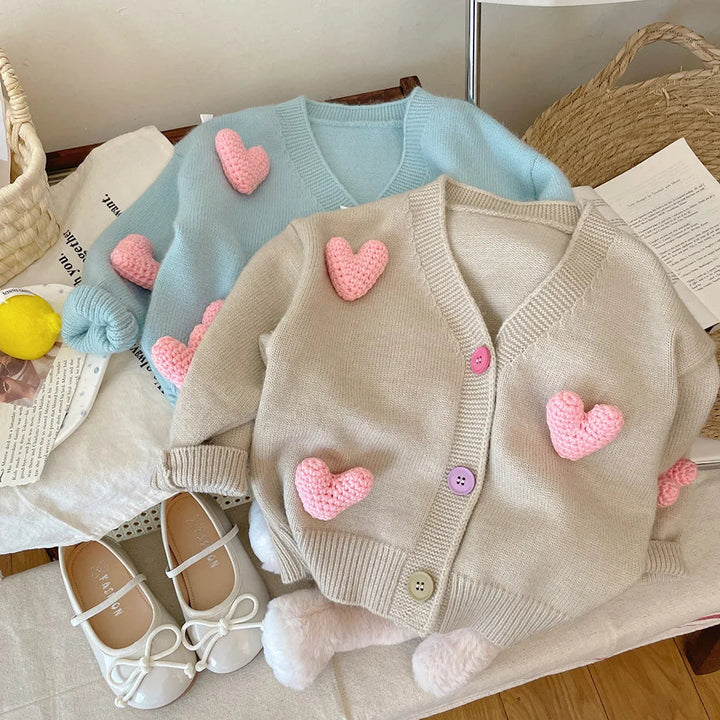 Blue and khaki knit cardigans with raised pink hearts and multicolored buttons
