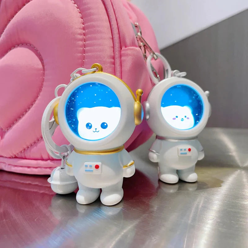 Two white astronaut charms with glowing blue helmets beside a pink bag
