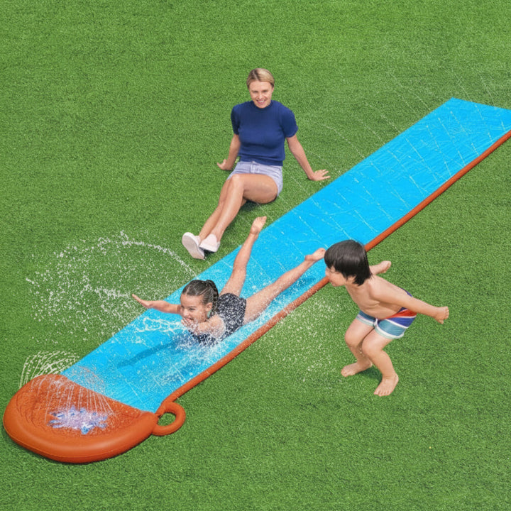 Children playing on a long blue water slide with an orange landing bumper on a lawn