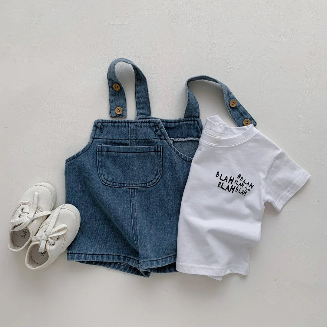 White printed T-shirt beside blue denim short overalls and white lace-up shoes